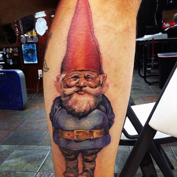 Tattoo of a classic garden gnome with a tall red hat, white beard, blue coat, and brown belt, standing with hands behind his back and a slight smile.