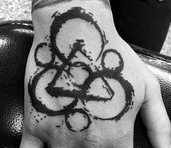 Coheed and Cambria Keywork tattoo on the hand with bold black ink and splatter effects, creating a striking and edgy look.