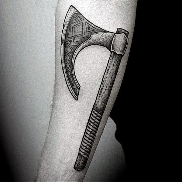 Black and grey Viking-style axe tattoo on the forearm, featuring intricate geometric patterns on the blade and a wrapped handle for a rugged look.
