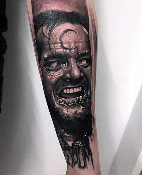Realistic black and grey tattoo of Jack Torrance from *The Shining*, featuring his deranged grin, intense shading, and eerie detailing for a haunting effect.