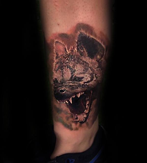 Realistic hyena tattoo on the lower leg, featuring an open mouth and sharp teeth, captured in a fierce, snarling expression.