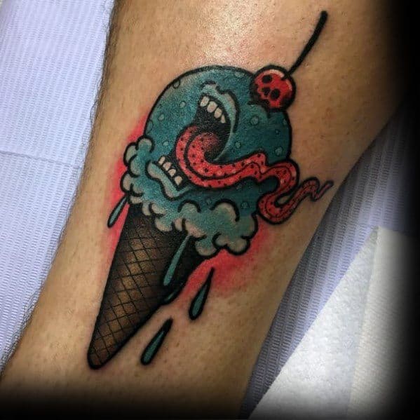 Bold tattoo of a blue ice cream cone with a monstrous mouth, sharp teeth, a long serpent-like tongue, and a skull-topped cherry.