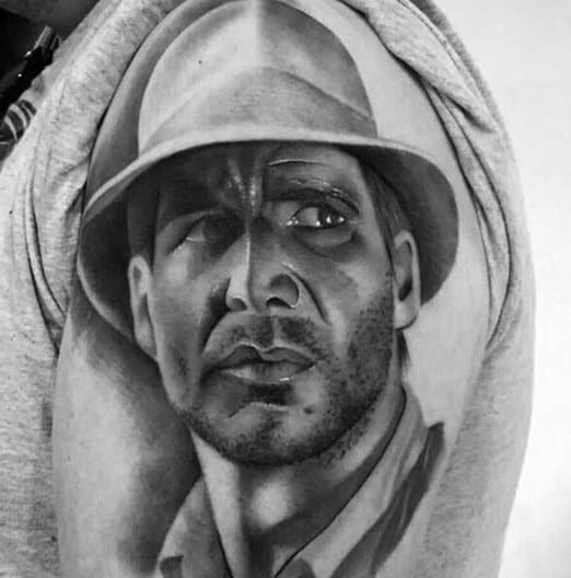 Realistic black and gray Indiana Jones tattoo capturing his intense gaze, rugged features, and iconic fedora in fine detail.