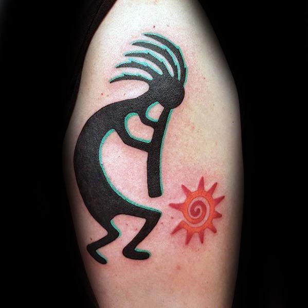 Simple black Kokopelli tattoo with teal accents, shown playing a flute beside a red spiral sun symbol on the upper arm.