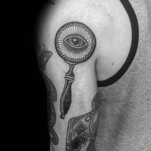 Tattoo of a magnifying glass with an eye in the center, featuring bold black outlines and intricate details for a mystical and symbolic design.