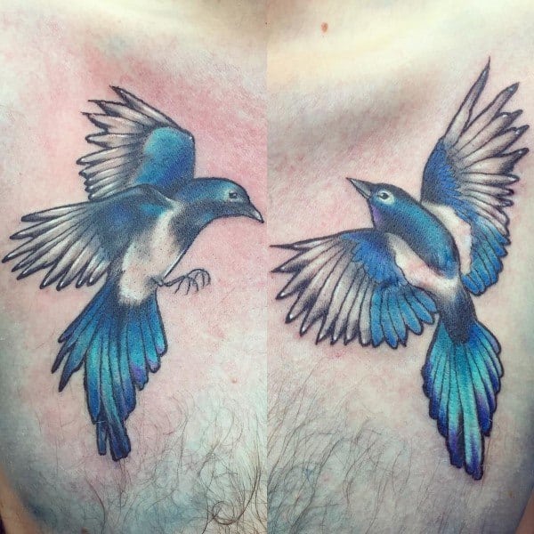 Colorful chest tattoo featuring two vibrant blue magpies in flight, symbolizing freedom, duality, and balance with dynamic wing positions.