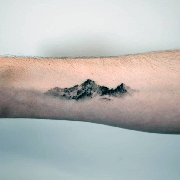 Realistic mountain tattoo on the forearm, featuring soft shading and a misty effect for a natural and subtle landscape design.