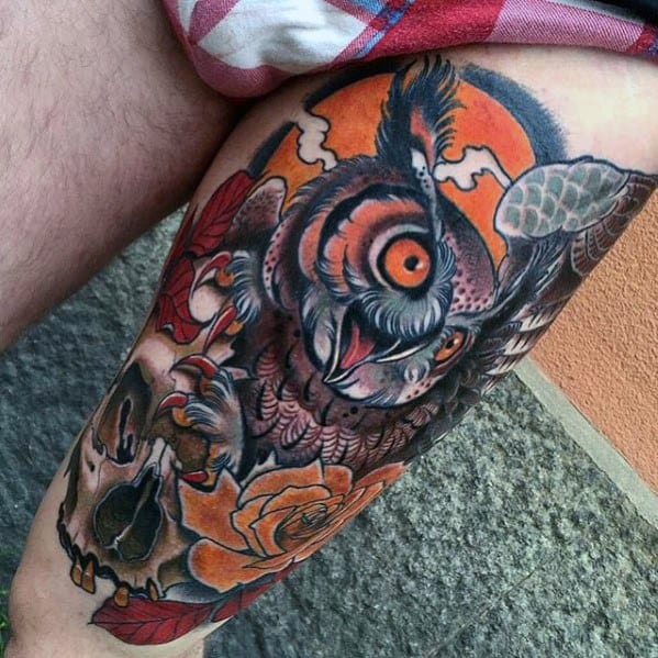 Neo-traditional owl tattoo with fierce orange eyes, bold shading, skull and rose details, and a dramatic sunset backdrop on the thigh.