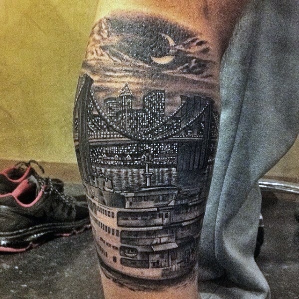 Realistic calf tattoo of the New York City skyline at night with a bridge, ferry, and crescent moon under dramatic clouds.