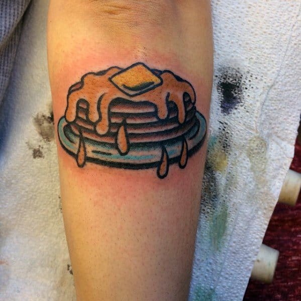 Classic pancake tattoo with dripping syrup and butter on a blue plate, featuring bold outlines and a traditional style for a fun design.