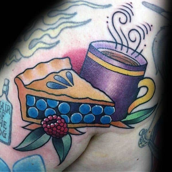 Blueberry pie tattoo with a steaming coffee cup, surrounded by leaves and a raspberry, creating a cozy, nostalgic, and traditional design