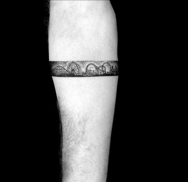 Black ink armband tattoo featuring a continuous roller coaster track with loops, Ferris wheel, and city skyline details.