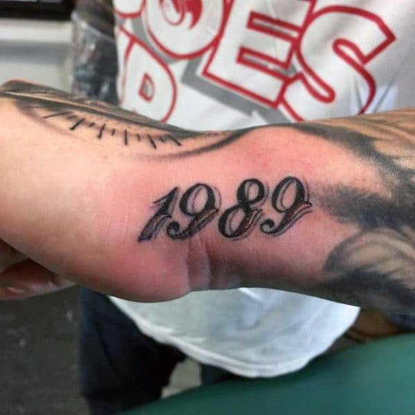 Side hand tattoo for men displaying the year 1989 in bold, black script across the outer edge of the hand.