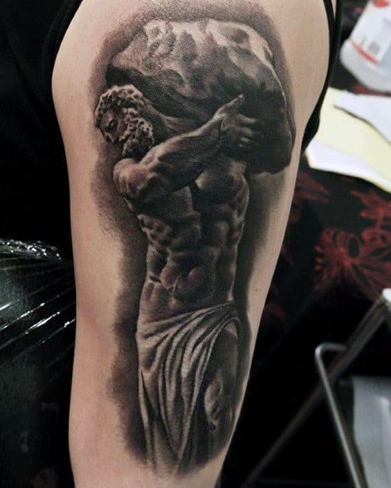 Realistic black and grey Sisyphus tattoo on upper arm, depicting him carrying a heavy boulder with detailed shading and muscle work.