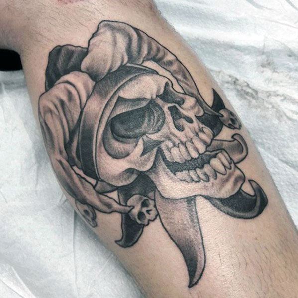 A black and gray tattoo of a skull wearing a jester hat, adorned with small skulls, creating a dark and playful design.