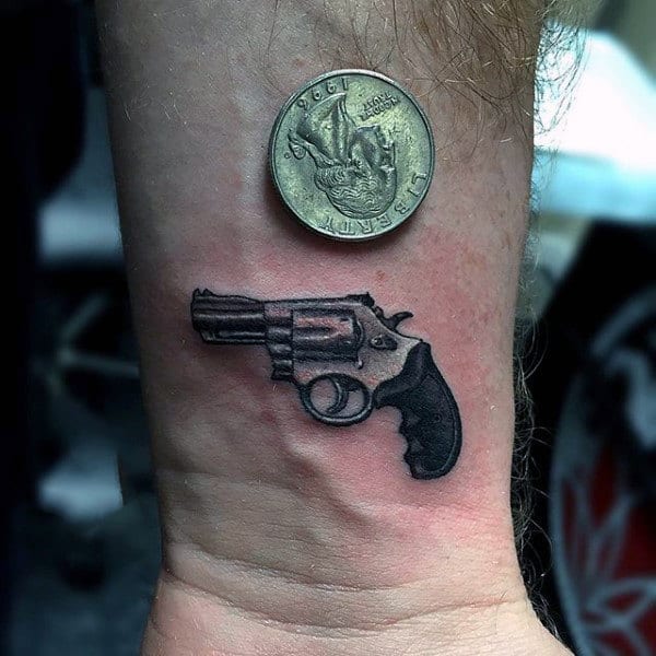 Guy With Small Pistol And 3D Coin Tattoo On Wrist