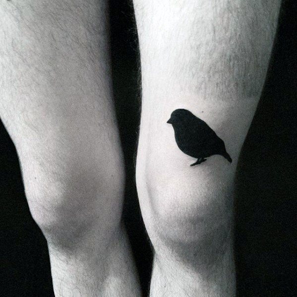 A tattoo of a small black bird inked on the inside of their left knee