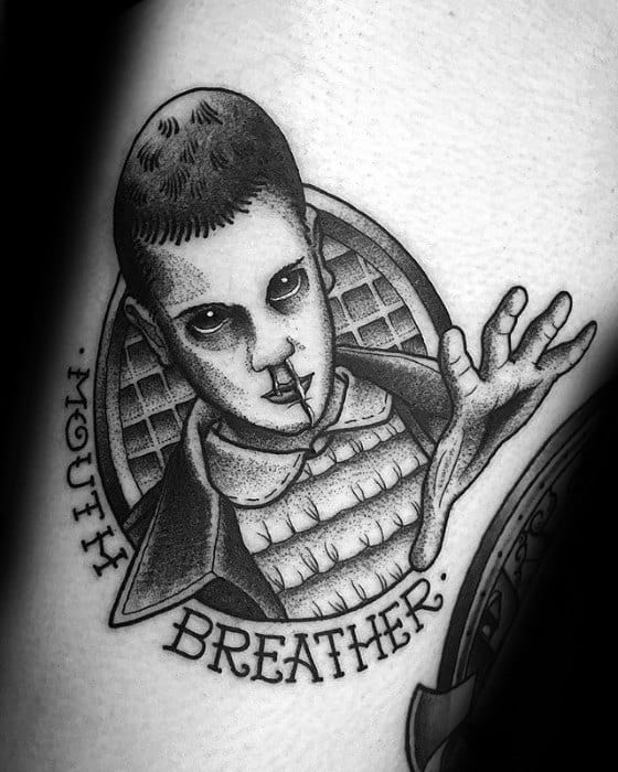 Black and grey tattoo of Eleven with a nosebleed and outstretched hand, captioned with the phrase “Mouth Breather” in bold lettering.