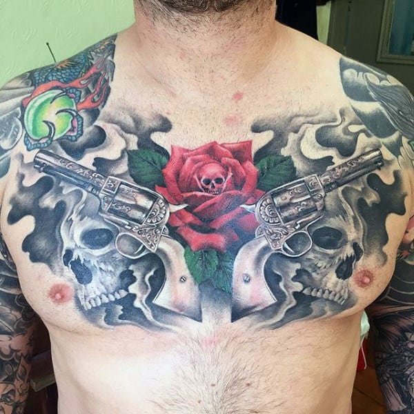 Guy With Striking Pistol Tattoo With Rose And Skulls On Chest