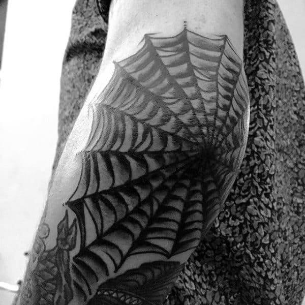 A black and white spider web tattoo on an elbow