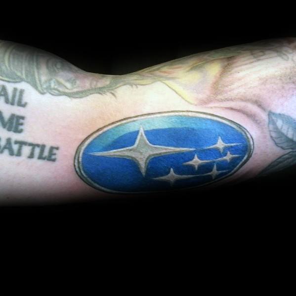 Blue and gold Subaru logo tattoo on the arm, featuring the iconic six-star emblem in an oval design with a realistic metallic effect.