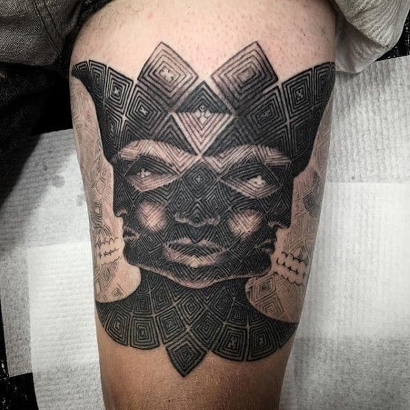Black and grey Tool-inspired tattoo on the thigh featuring a multi-faced head with geometric patterns, symmetry, and hypnotic detail.