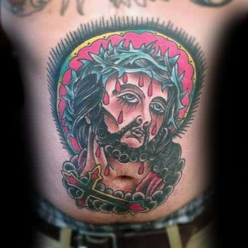 Bold traditional tattoo of Jesus with a crown of thorns, red teardrops, and a radiant pink and yellow halo, placed centrally on the torso.
