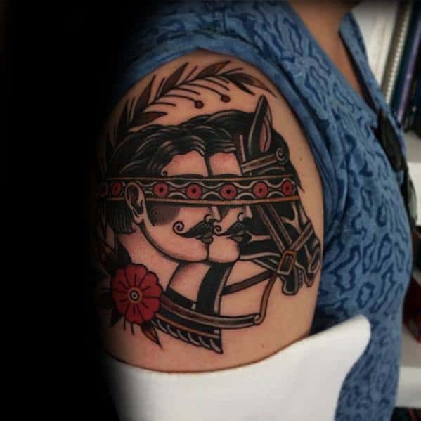 Traditional upper arm tattoo of a blindfolded man and horse facing forward, framed by bold lines, leaves, and a red flower.