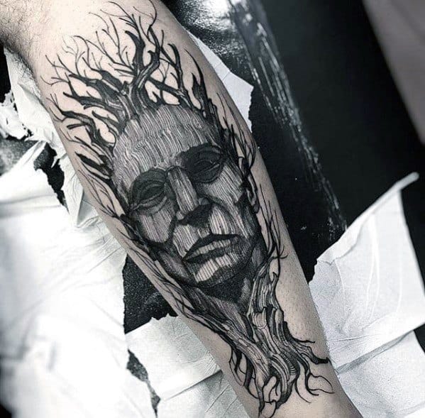 Black and grey tattoo of a tree merging with a human face, symbolizing a deep connection to nature, wisdom, and transformation.