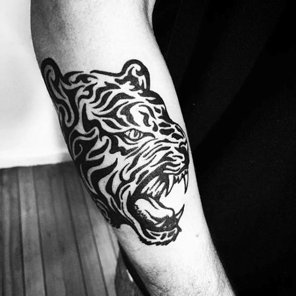 Black and white tattoo of a roaring tiger's head in a tribal design on an arm