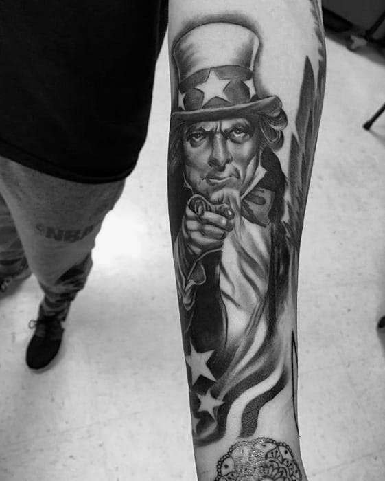 Realistic black and gray Uncle Sam sleeve tattoo with intense shading, finger pointing pose, and flowing American flag detail.