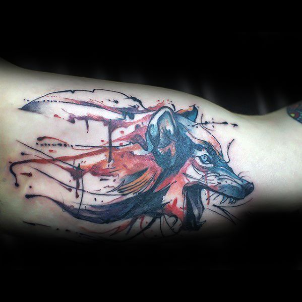 Watercolor-style tattoo of a wolf's head with splashes of red and blue ink