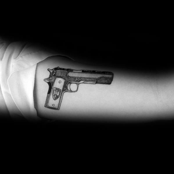 Small black and gray tattoo of a 1911 pistol on the inner arm, featuring fine details and a custom grip design for a minimalist yet bold look.