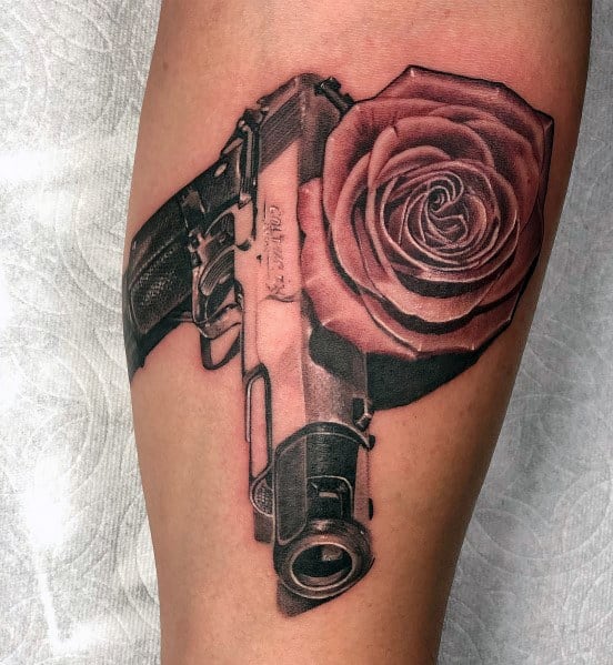 Realistic black and gray tattoo of a 1911 pistol with a detailed rose, blending bold shading and fine details for a striking design on the arm.
