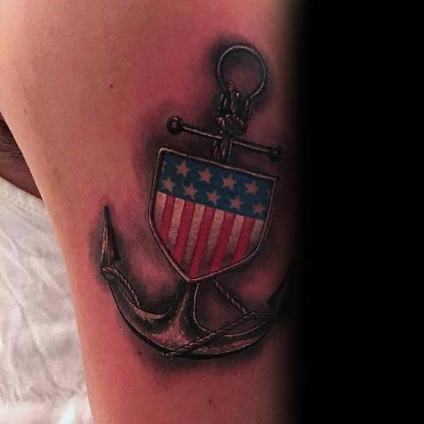 Tattoo of an anchor with a shield displaying the American flag on an upper arm
