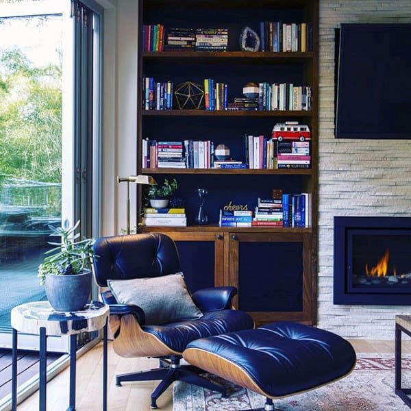 Contemporary living space with a sleek leather lounge chair, bookshelf, fireplace, and large windows.