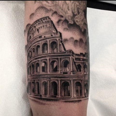 A detailed tattoo of the Roman Colosseum on a forearm with a gladiator standing in the foreground against a cloudy sky background