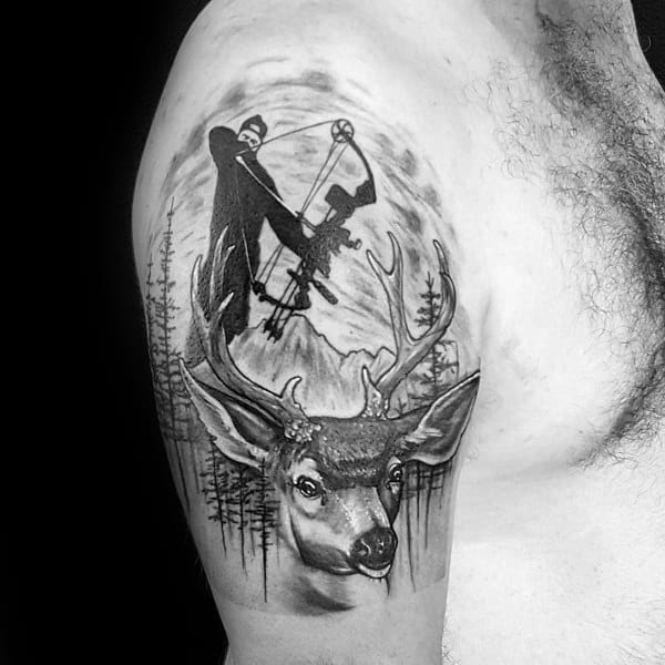 Black and grey upper arm tattoo of a realistic buck in the forest with a silhouette of a bowhunter aiming above, set against mountain scenery.