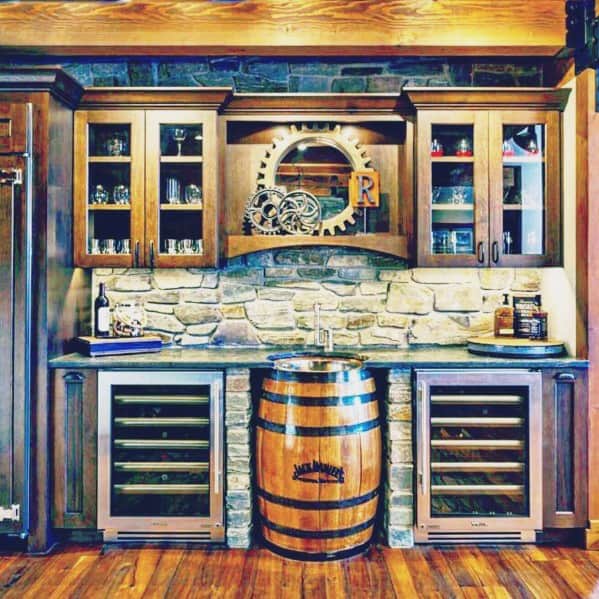 Rustic home bar with wooden cabinetry, stone backsplash, and a barrel sink flanked by wine refrigerators