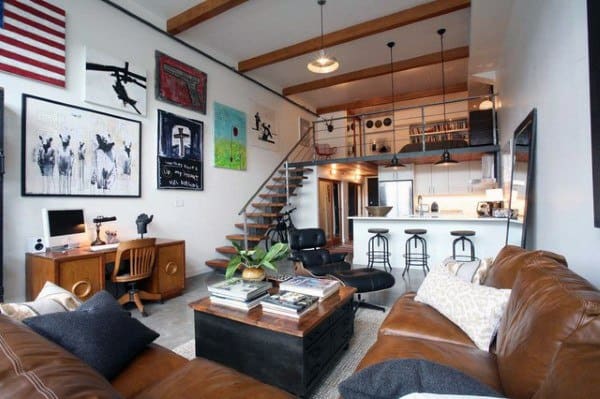 Industrial loft with leather sofas, art-covered walls, and mezzanine overlooking open kitchen area.
