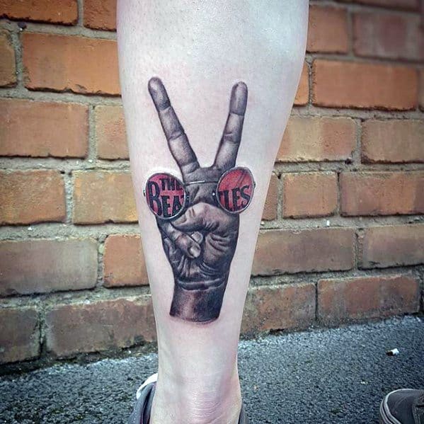 Realistic forearm tattoo of a hand making the peace sign, with circular red sunglasses reflecting "The Beatles" logo in each lens.
