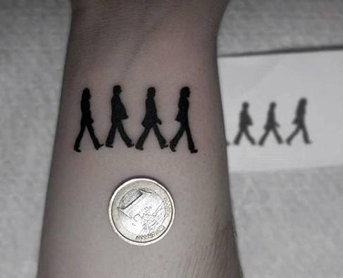 Tiny silhouette tattoo of The Beatles walking across Abbey Road, placed near the wrist and shown next to a coin for size comparison.