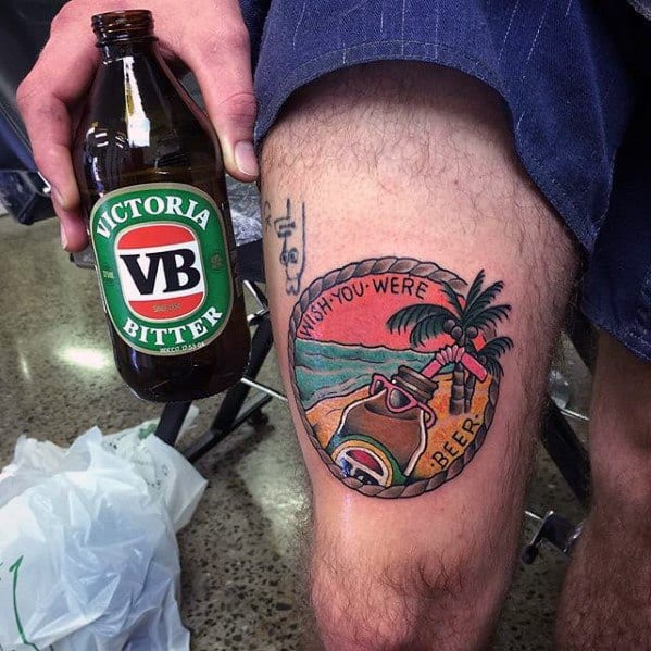 Colorful thigh tattoo inspired by Victoria Bitter, featuring a beach scene with a tipped beer bottle and the phrase "Wish you were beer" in bold lettering.