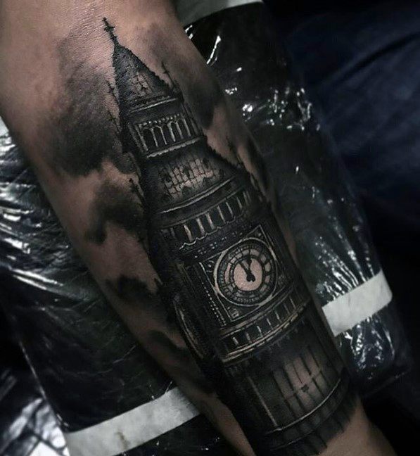 Detailed black and grey tattoo of Big Ben, surrounded by dramatic cloud shading, covering the forearm with intricate details of the clock and architecture.