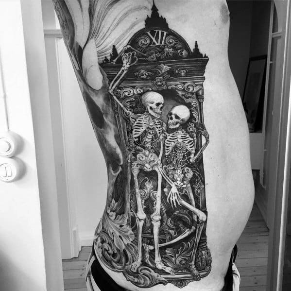 Black and grey ribcage tattoo featuring two skeletons inside an ornate grandfather clock, detailed shading, and swirling elements for a gothic-inspired design.