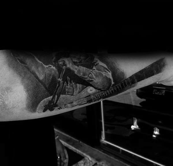 Black and gray inner arm tattoo of Bob Marley mid-performance, holding a guitar and singing with dynamic shading and movement.