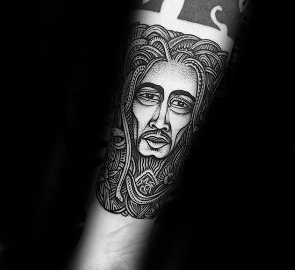 Bob Marley tattoo in a stylized blackwork design with intricate patterns and bold lines forming his face and dreadlocks on the forearm.