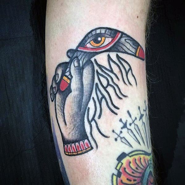 Boomerang tattoo with an eye motif, held by a hand, and the word KARMA written in stylized script across the forearm.