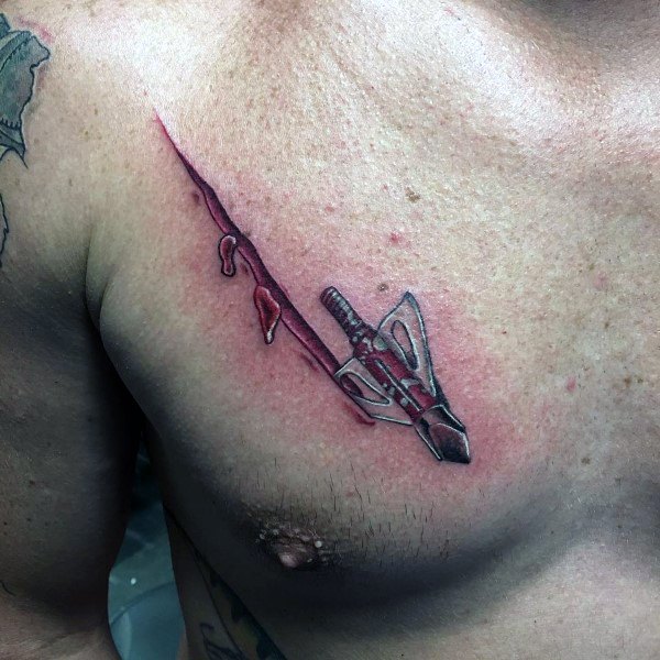 Realistic chest tattoo of a broadhead arrow appearing to pierce through the skin, with red ink simulating blood and torn flesh.