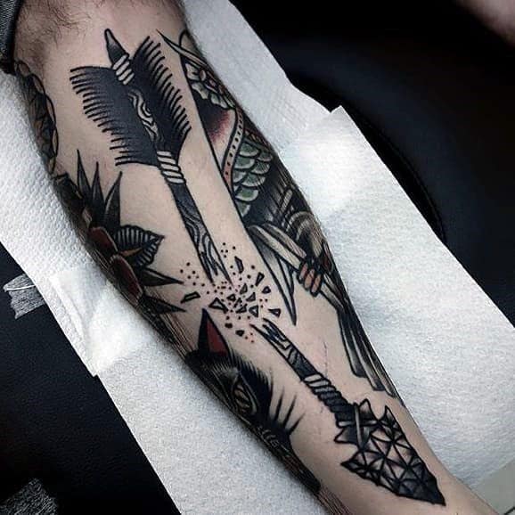 Bold traditional broken arrow tattoo with thick black outlines, geometric tip, and explosive shards at the break point, placed on the forearm.